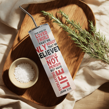 Load image into Gallery viewer, Lifestyle photo of the John 3:16 Cross™ tumbler placed on a rustic table with warm background lighting.